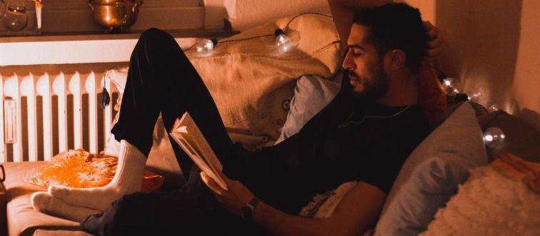 Man lounging on couch reading book 